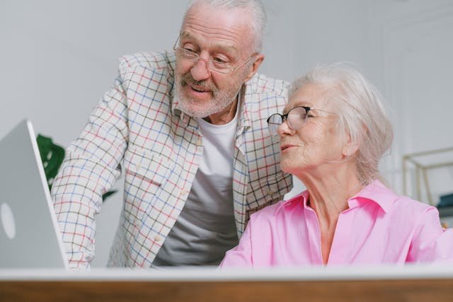 Senior couple smiling while reviewing retirement fund growth and financial planning documents on a laptop at home.